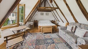 A cozy attic bedroom with a sloped ceiling, a wooden bed, a patterned rug, a sofa, and a small table with a chair. - Shared pool and wooded grounds - house for 4 (Montignac)