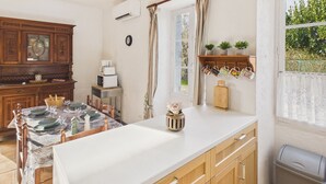 Une cuisine avec des meubles en bois, un plan de travail blanc, une table à manger pour quatre personnes et une fenêtre avec des rideaux.