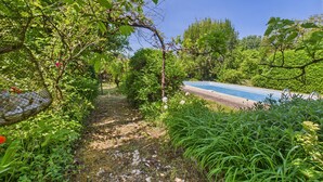 Un sentier de jardin qui mène à une piscine entourée d’une végétation luxuriante et d’arbres.