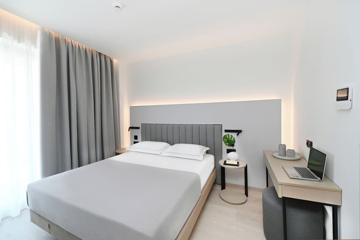 A modern hotel room with a large bed, a desk with a laptop, and a small side table.