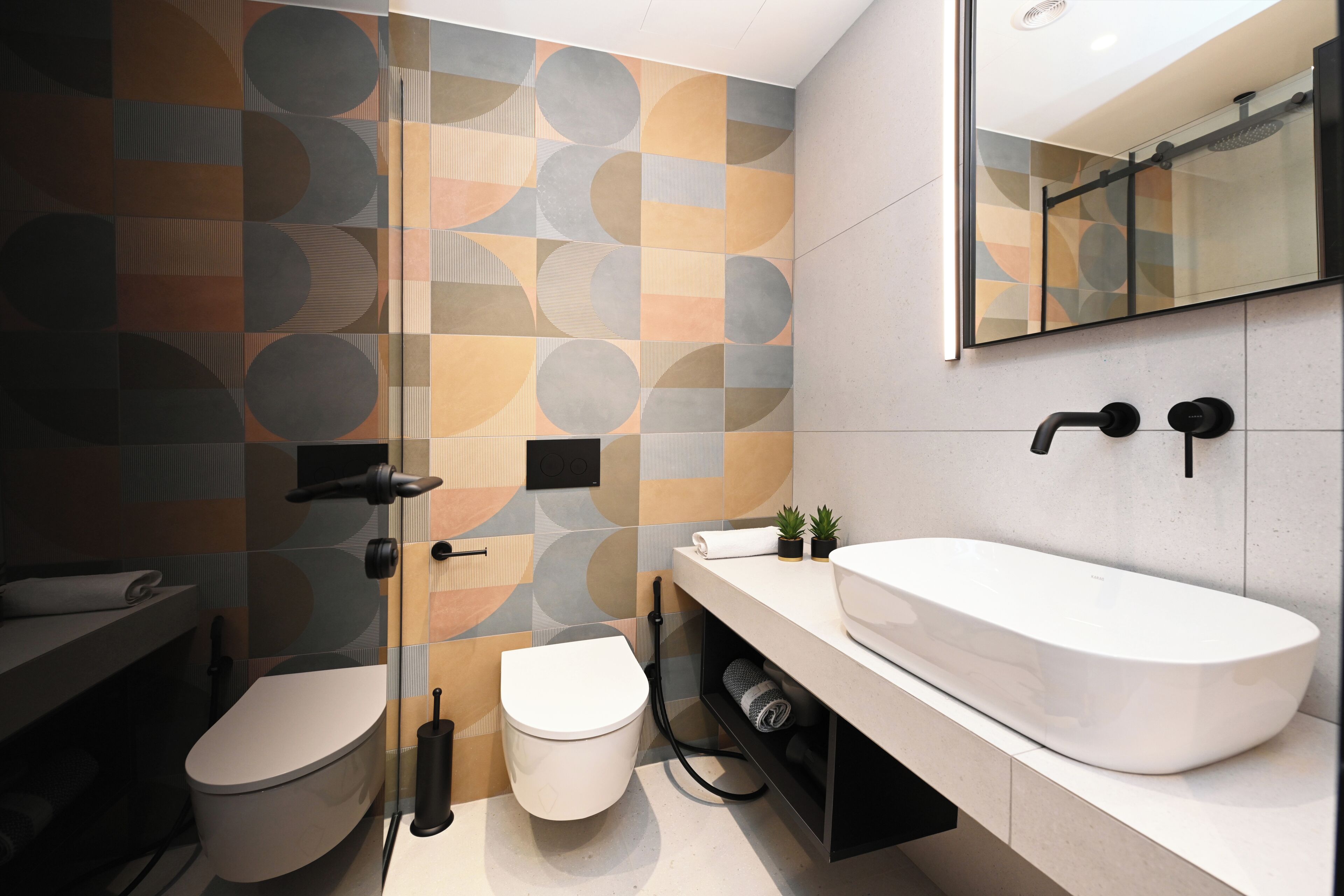A modern bathroom with a geometric tile backsplash, a white sink, and a toilet.
