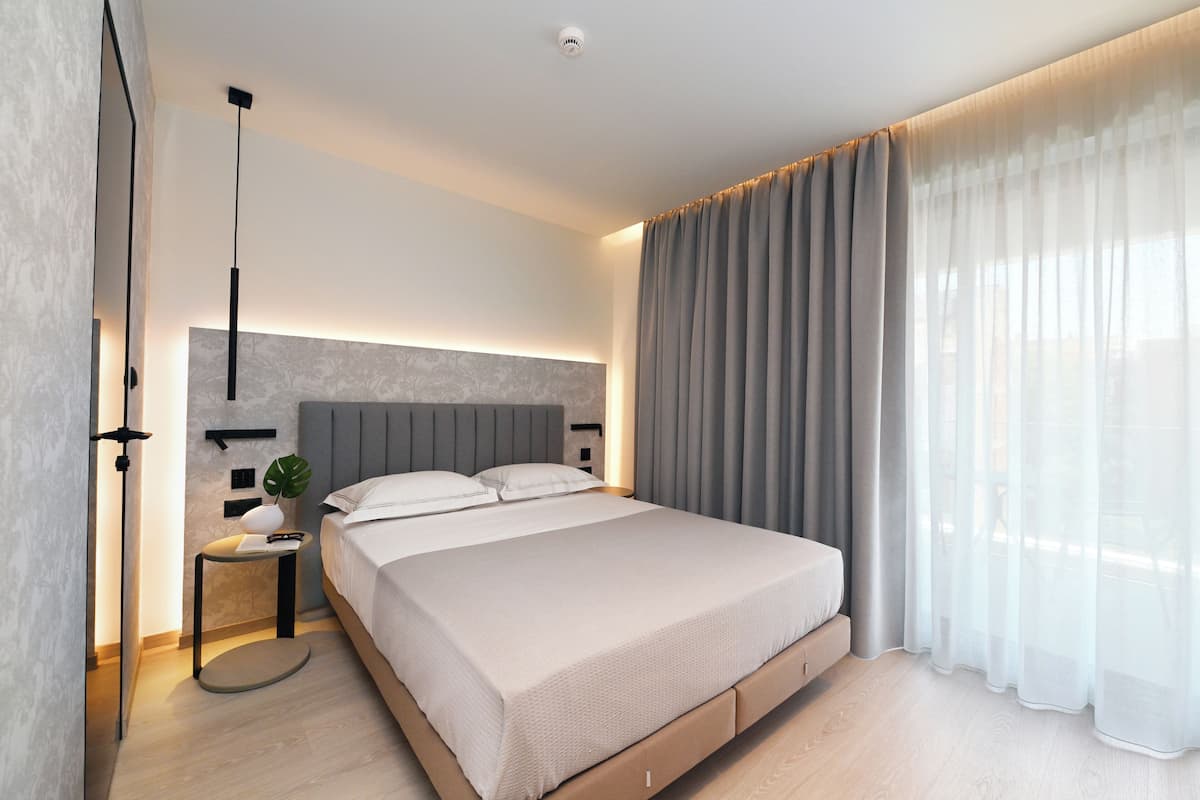 A modern bedroom with a bed, bedside table, lamp, and curtains.