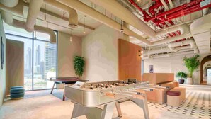 A modern indoor space with a foosball table, large windows, and industrial-style ceiling pipes. - Prime Studio w Burj Views Near Downtown and Canal (Dubai)