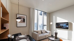 A modern living room with a dining area, a sofa, a TV, and a large window with curtains. - Prime Studio w Burj Views Near Downtown and Canal (Dubai)