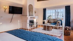 Un dormitorio con cama, chimenea, televisor y vista al exterior.