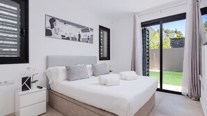 Un dormitorio con cama, mesita de noche, un cuadro enmarcado y vistas al exterior.