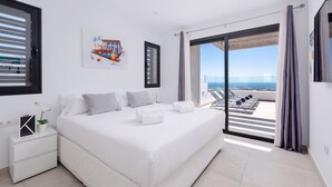 Un dormitorio moderno con una cama grande, una mesita de noche, un cuadro y vistas a un balcón con tumbonas.