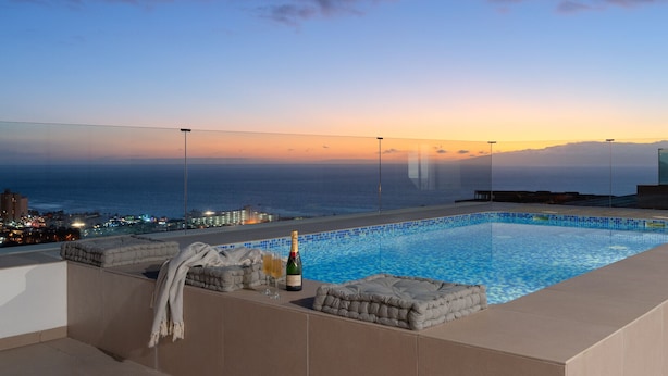 Una piscina infinita en la azotea con vista al atardecer, sillones de descanso y una botella de champán.