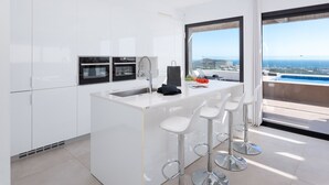 Una cocina moderna con una isla central, taburetes de bar y vista al océano.