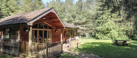A rustic cabin with a porch and a picnic table in a wooded area.