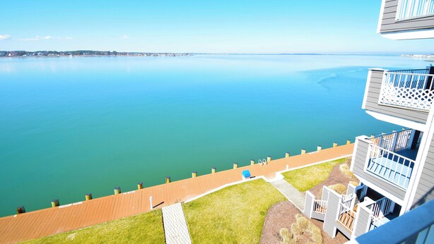 A waterfront property with a wooden deck, a grassy area, and a view of the water.