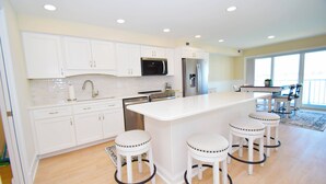 A modern kitchen with white cabinets, stainless steel appliances, and a central island with bar stools.