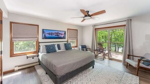 A bedroom with a large bed, a ceiling fan, a TV, and a view of greenery through the windows. - Tamarack Lodge Lake Tomahawk WI (Lake Tomahawk)