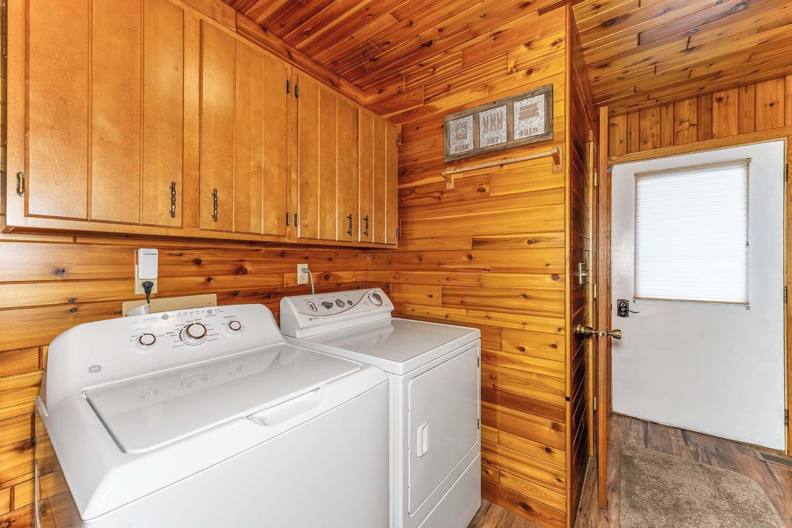 A laundry room with wooden walls and cabinets, a washing machine, and a dryer.