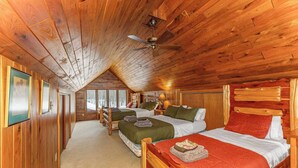 A log cabin bedroom with two beds, a ceiling fan, and a large window.