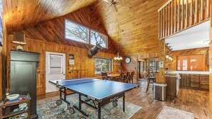 A spacious room with a ping pong table, wooden walls, and a large window.