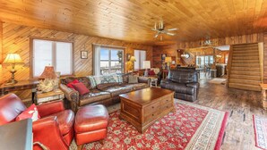 A spacious living room with a wooden ceiling, leather sofas, a wooden coffee table, and a red patterned rug.