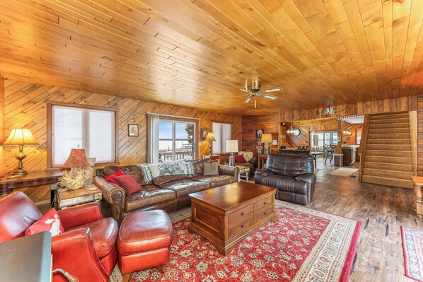 A spacious living room with a wooden ceiling, leather sofas, a wooden coffee table, and a red patterned rug.