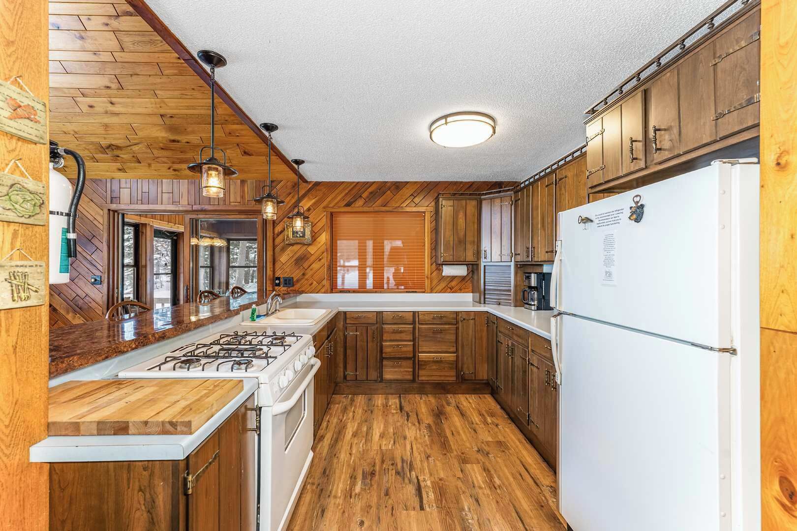 A kitchen with wooden cabinets, a stove, a refrigerator, and pendant lighting.