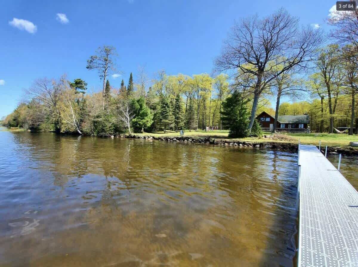 A riverside view with a dock extending into the water, surrounded by trees and a cabin.
