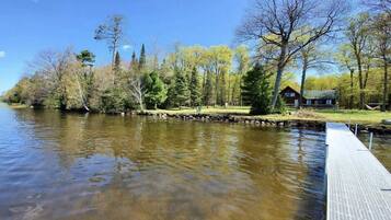 A riverside view with a dock extending into the water, surrounded by trees and a cabin.