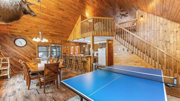 A wooden interior with a ping pong table, dining area, kitchen, and staircase.
