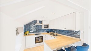 Una cocina compacta con armarios blancos, encimera de madera, microondas integrado y un lavabo.