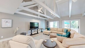 Un salon spacieux avec un grand canapé d’angle, un téléviseur à écran plat et un ventilateur de plafond.