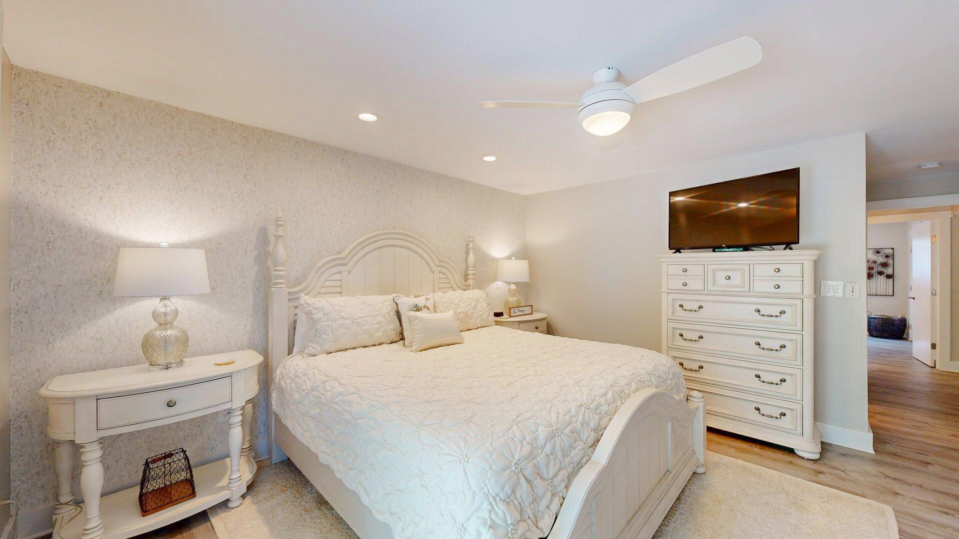 A bedroom with a bed, nightstands, a dresser, a ceiling fan, and a TV.