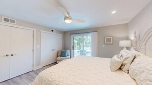 Une chambre avec un grand lit, un ventilateur de plafond et une porte-fenêtre coulissante donnant sur l’extérieur.