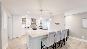 Une cuisine moderne avec des meubles blancs, un îlot central doté de tabourets et des luminaires suspendus.