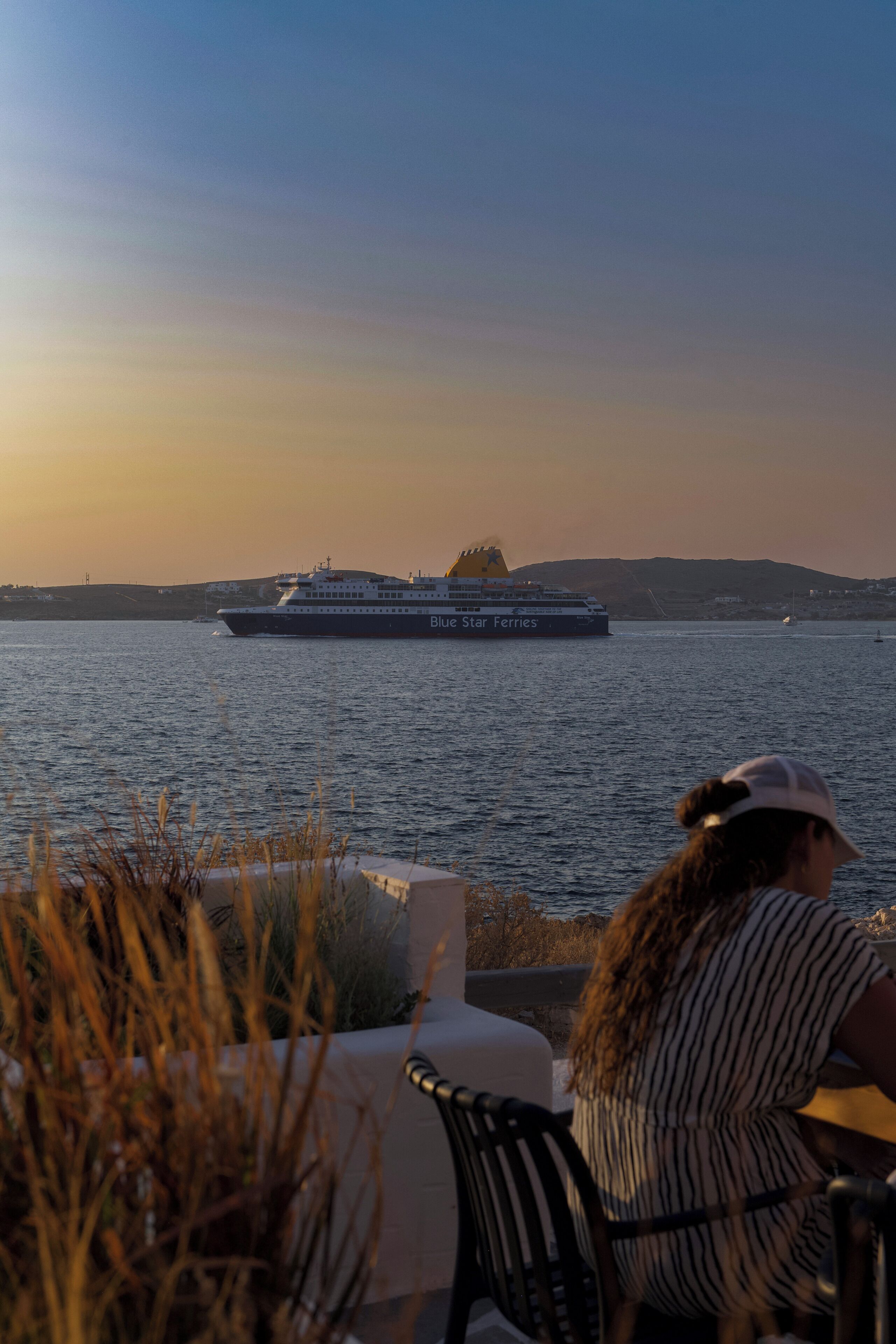 A ferry named Blue Star Ferries on a body of water with a person seated at a table in the foreground.