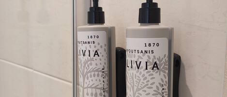 Two white bottles of Ivia white tea scented shower gel and lavender scented shower gel mounted on a tiled wall.
