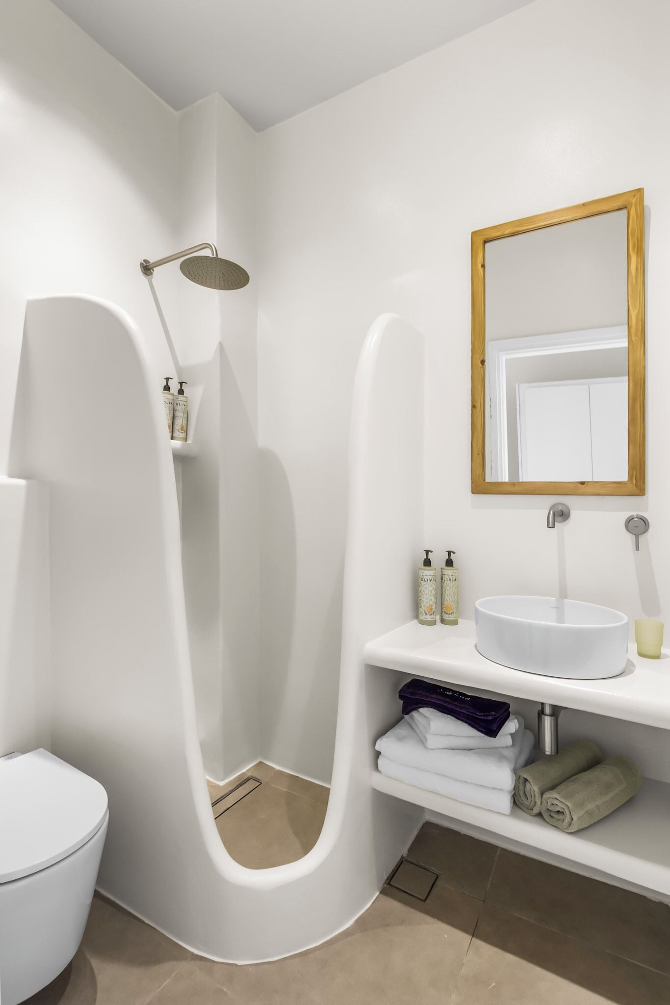 A modern bathroom with a white sink, a shower with a handheld showerhead, a toilet, and a mirror with a wooden frame.