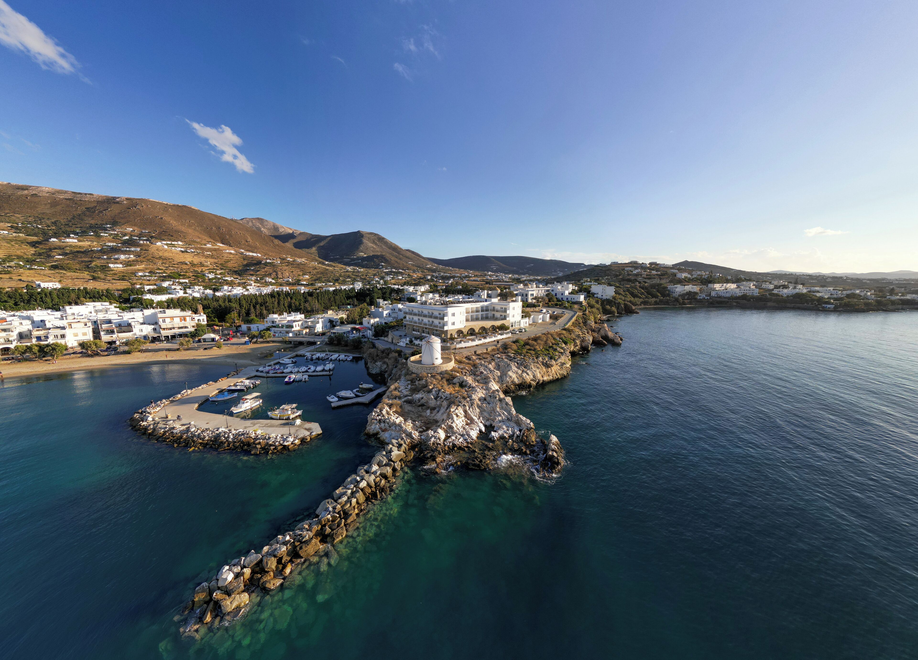 Un pueblo costero con edificios blancos, un puerto deportivo y aguas azul cristalino.