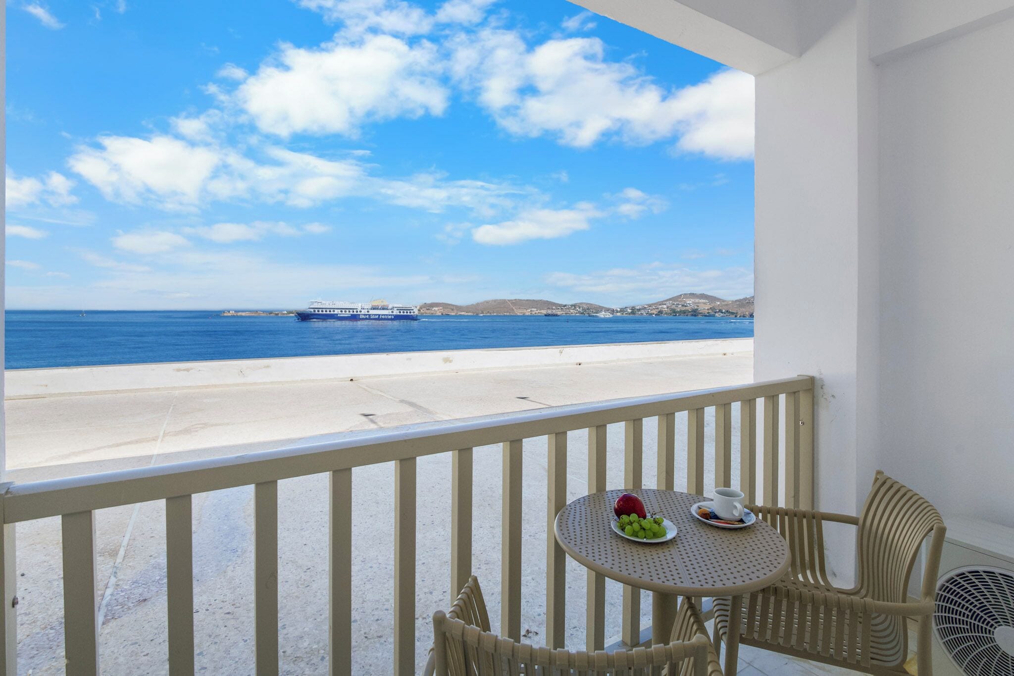 A balcony with a table and chairs overlooking a beach and the sea.