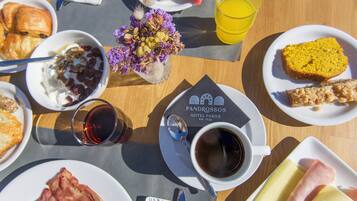 Una mesa de desayuno con croissants, yogur con frutos rojos, una rebanada de sandía, un vaso de jugo de naranja, una taza de café y un plato con jamón y queso.