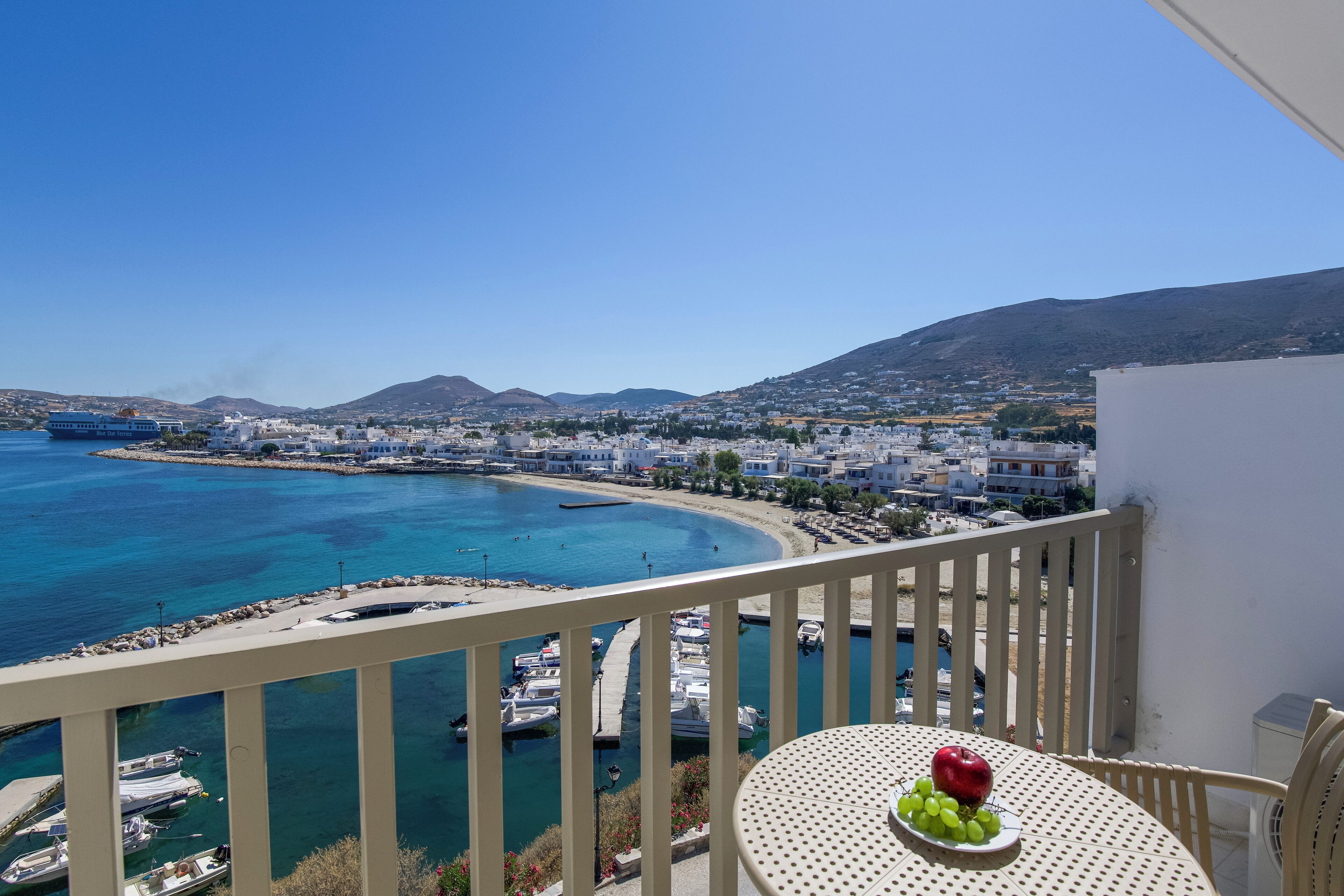 Un balcon avec une table, une vue sur une ville côtière et des bateaux sur l’eau.