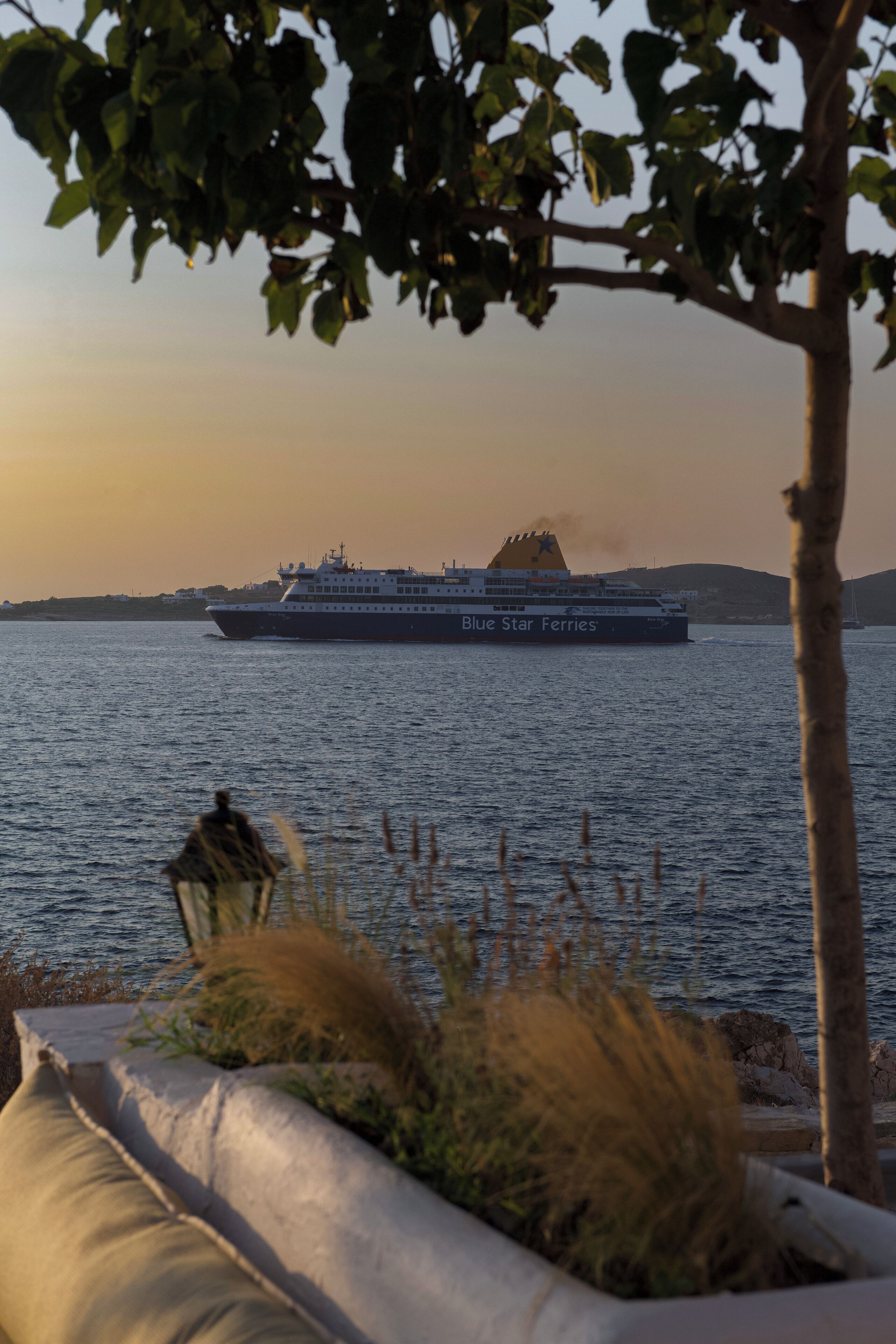 Eine Fähre namens Blue Star Ferries auf dem Wasser, mit Blick auf eine Küstenlandschaft im Hintergrund.
