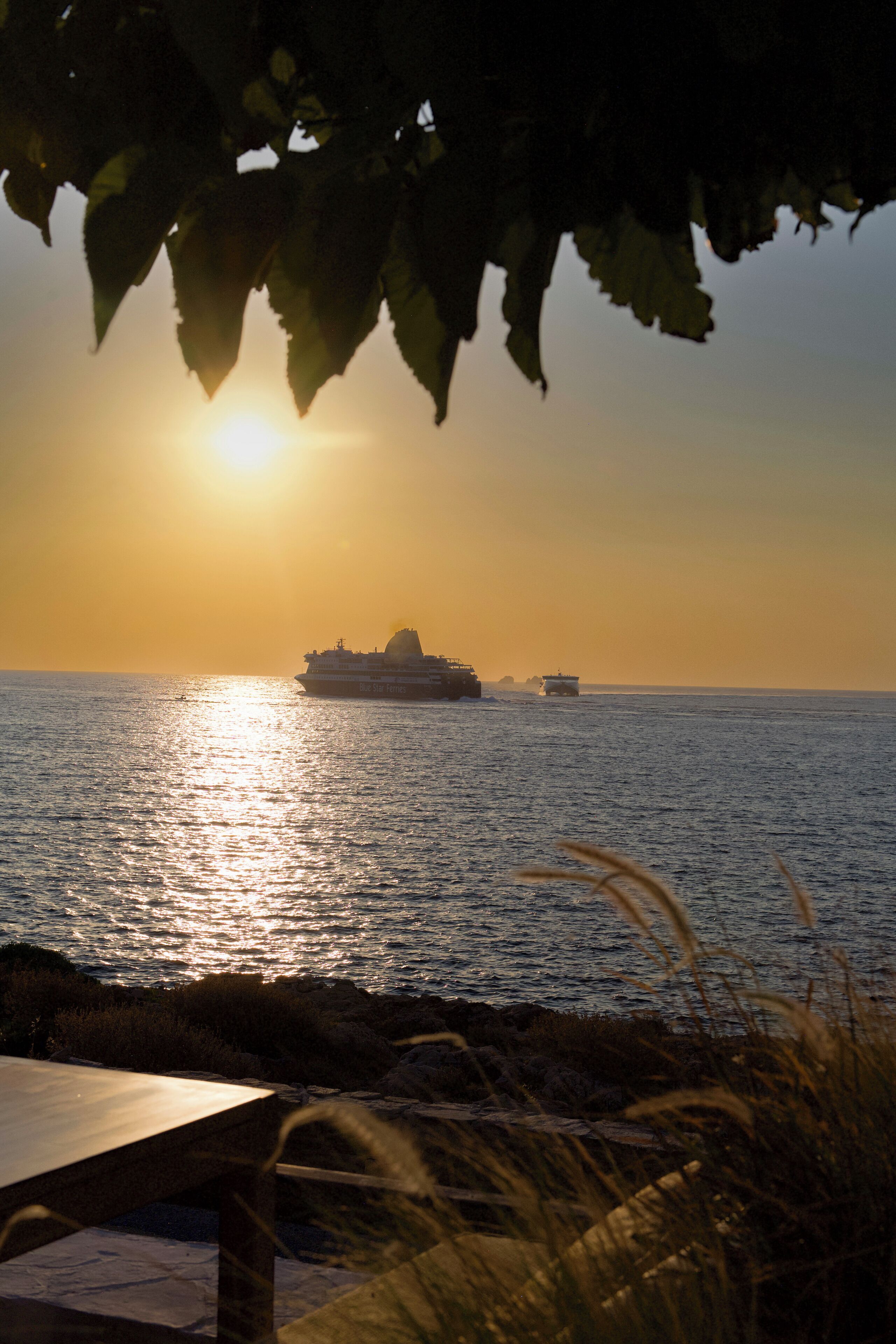 A sunset over a calm sea with a cruise ship and a smaller boat in the distance.