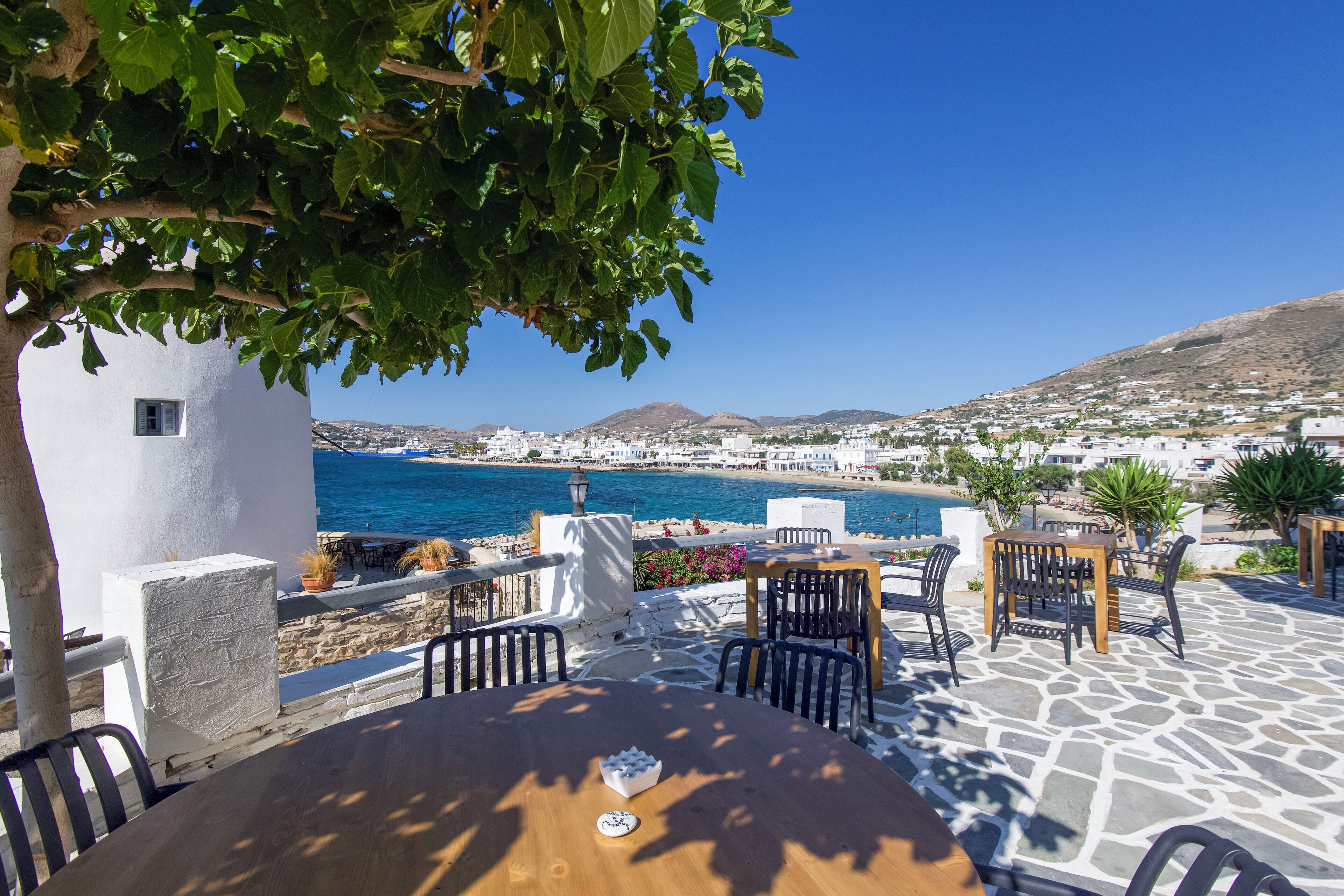 A seaside patio with stone flooring, outdoor seating, and a view of the sea and town.