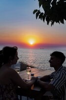 A sunset view from a table overlooking the sea, with a glass of wine on the table.