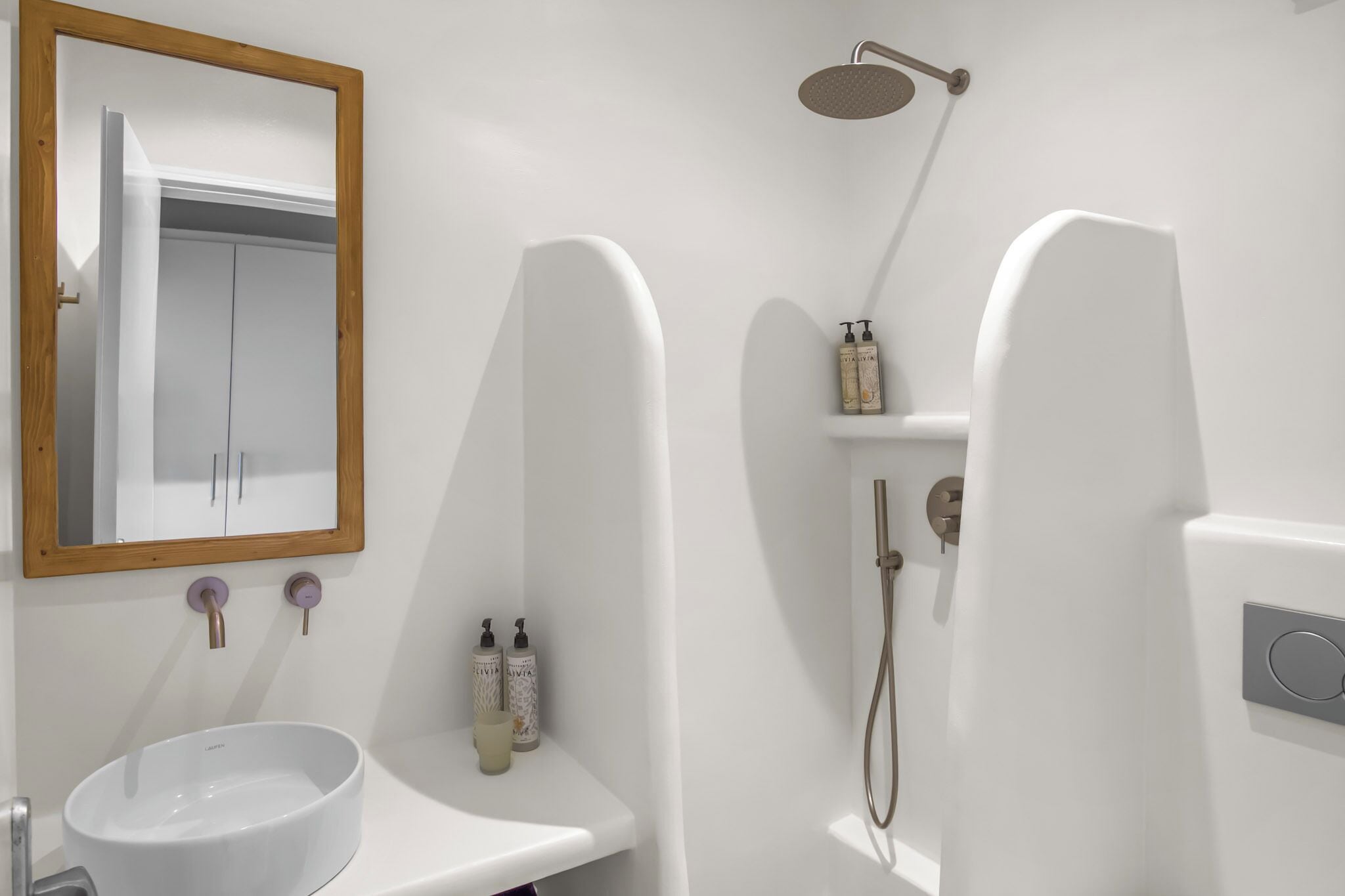 A bathroom with a white sink, a mirror with a wooden frame, and a shower with a handheld showerhead.