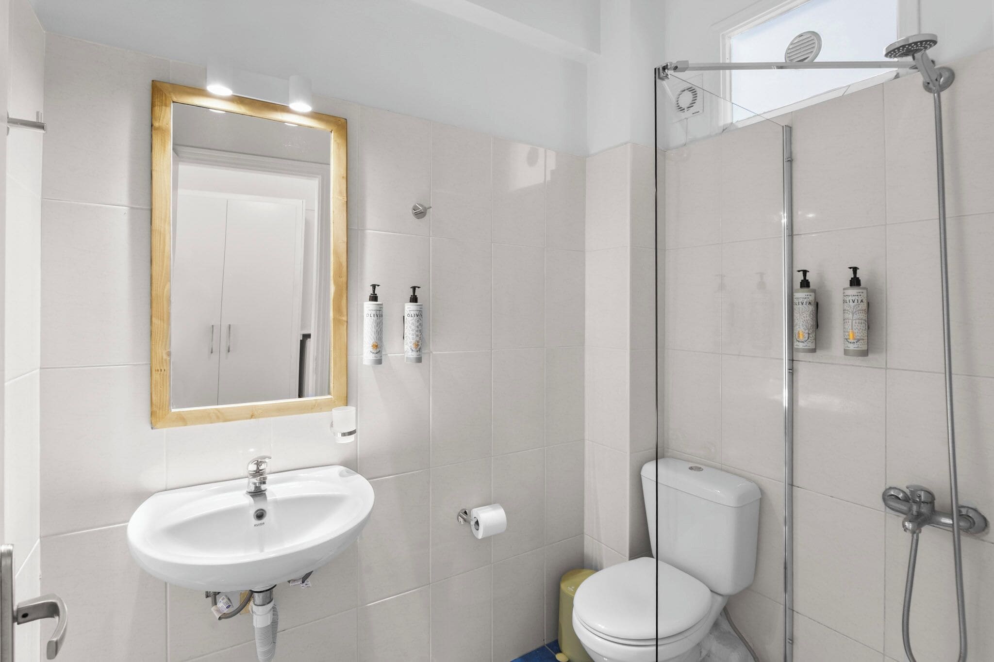 Une salle de bain moderne avec un lavabo, un miroir et des toilettes blancs, ainsi qu’un espace de douche clos par des parois de verre.
