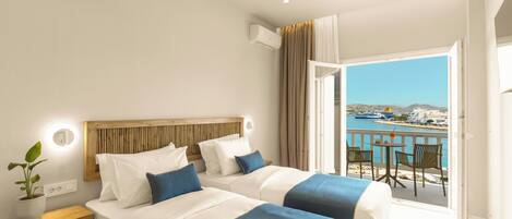 A hotel room with two beds, a balcony with a view of the sea, and a potted plant on the nightstand.
