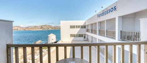 Un balcón de hotel con vistas al mar, que incluye una mesa redonda y sillas, y un cartel que dice "Hotel Pandrossos".