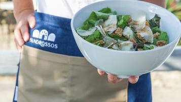 Una persona sosteniendo un bol de ensalada, usando un delantal azul con el logotipo 'ANDROSSOS'.