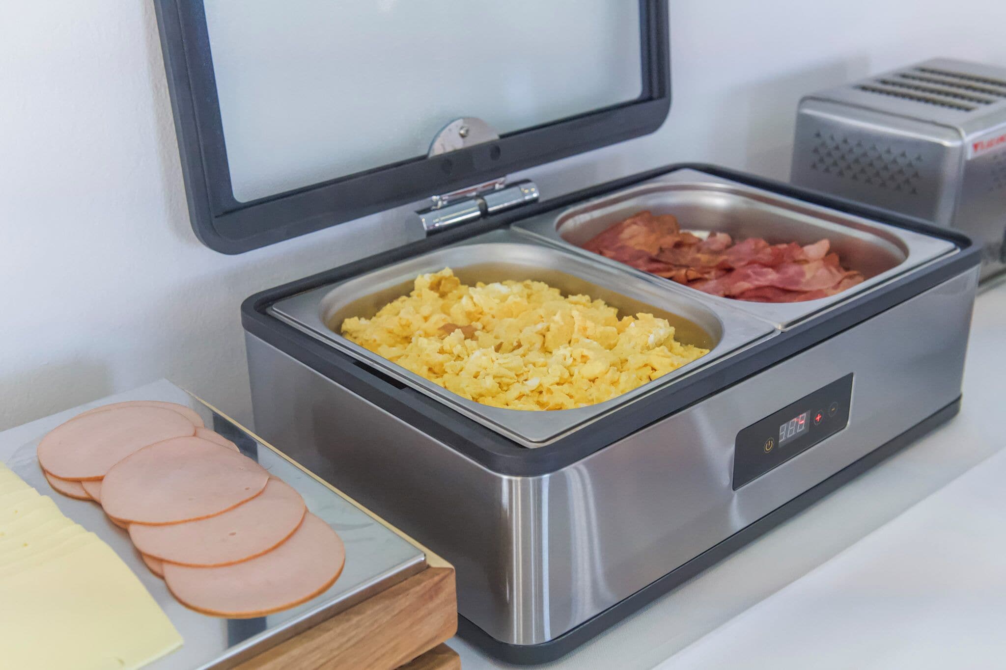 Un bufé con huevos revueltos, tocino y jamón en rodajas.
