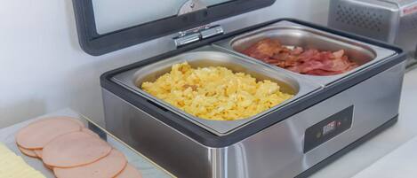 Un bufé con huevos revueltos, tocino y jamón en rodajas.