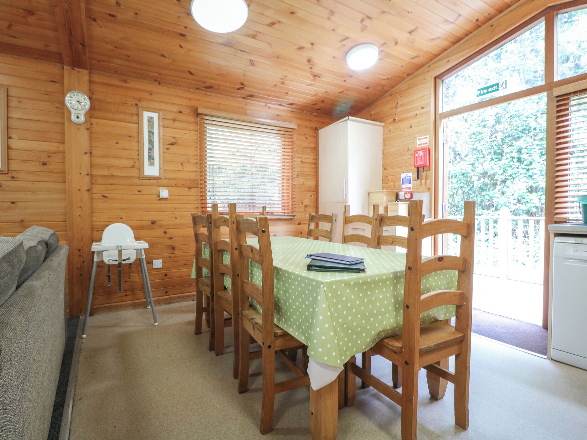 Una cabaña de madera con una mesa de comedor, sillas, un reloj y un letrero de salida de incendios.